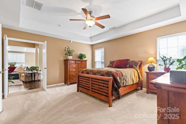 bedroom featuring visible vents, a raised ceiling, and light colored carpet