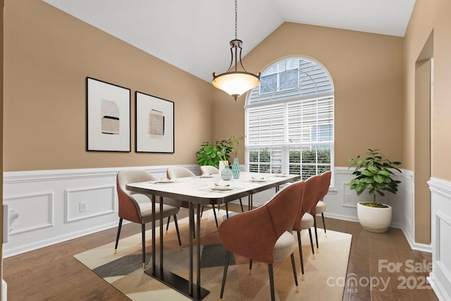 dining area with a wainscoted wall, vaulted ceiling, a decorative wall, and wood finished floors