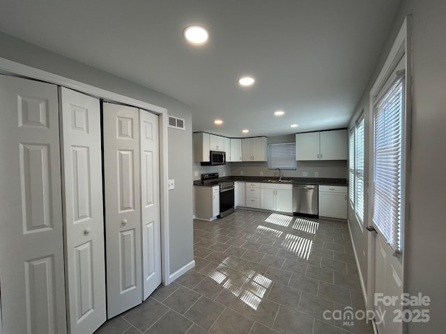 kitchen featuring dark countertops, stainless steel appliances, white cabinetry, a sink, and recessed lighting