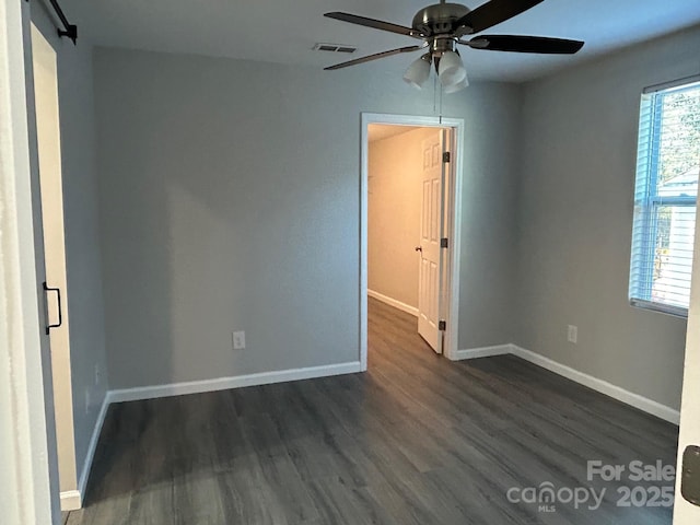 unfurnished bedroom featuring a barn door, dark wood-style flooring, visible vents, and baseboards