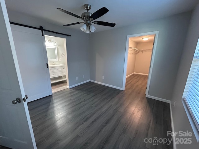 unfurnished bedroom featuring a barn door, a spacious closet, baseboards, and dark wood-type flooring