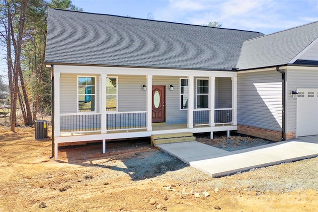 view of front of house with an attached garage, a porch, cooling unit, and roof with shingles