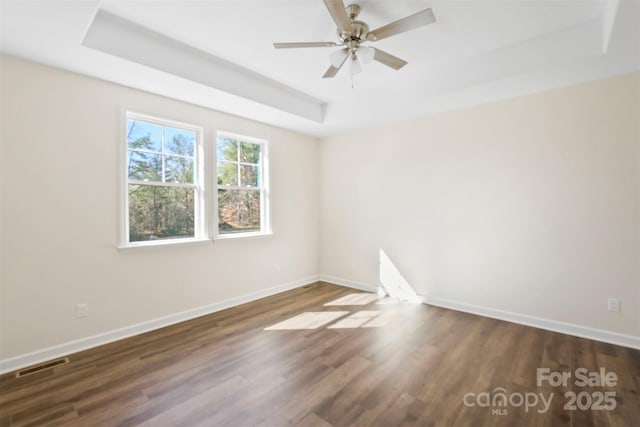 spare room featuring a raised ceiling, visible vents, and baseboards