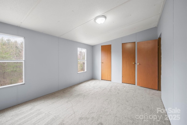 unfurnished bedroom with carpet floors, vaulted ceiling, and two closets