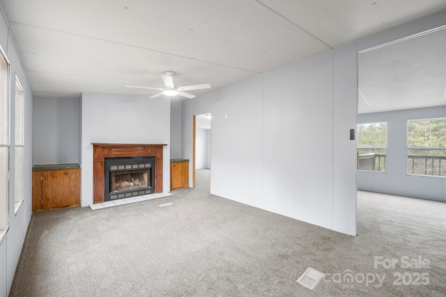 unfurnished living room with carpet, visible vents, a ceiling fan, and a fireplace with flush hearth