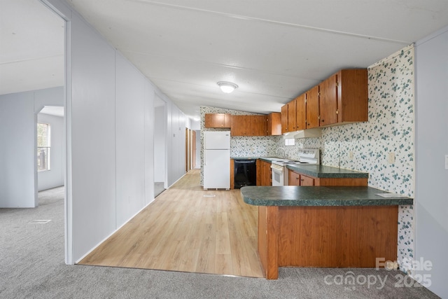 kitchen featuring light carpet, white appliances, dark countertops, brown cabinets, and a peninsula