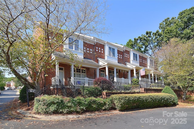 townhome / multi-family property with brick siding, a fenced front yard, and a porch