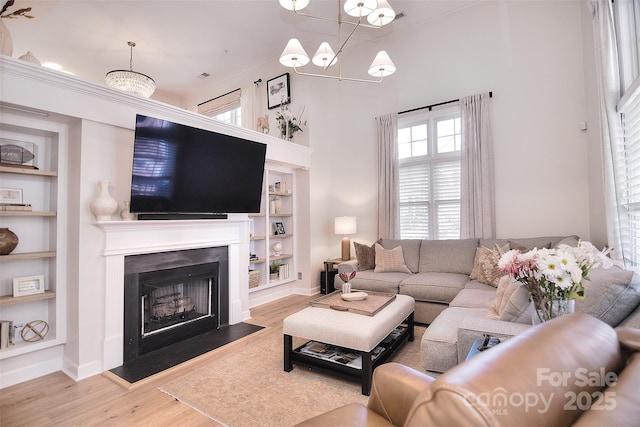 living area with built in shelves, a notable chandelier, a fireplace with flush hearth, wood finished floors, and baseboards