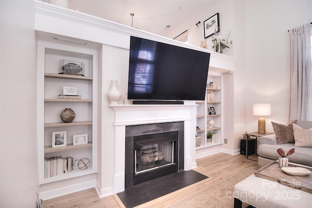 living room with a fireplace with flush hearth, baseboards, built in shelves, and wood finished floors