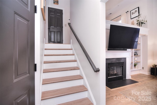 stairway featuring a fireplace with flush hearth, baseboards, and wood finished floors