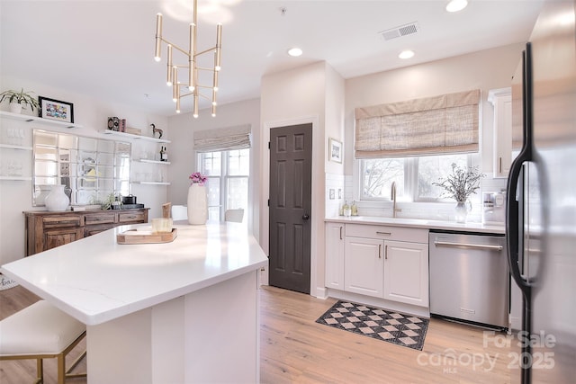 kitchen with visible vents, white cabinets, a center island, stainless steel appliances, and light wood-type flooring