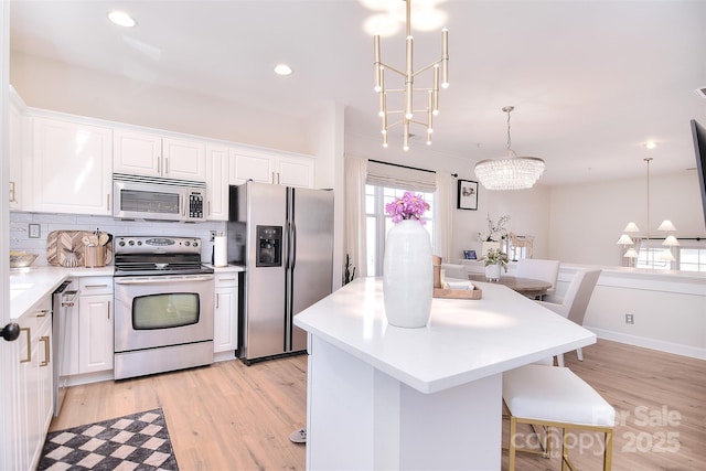 kitchen with tasteful backsplash, white cabinets, a kitchen island, an inviting chandelier, and stainless steel appliances