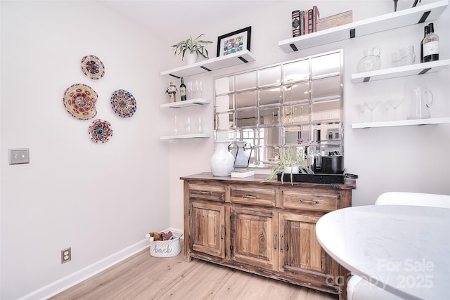 bar featuring baseboards, light wood-style flooring, and wet bar