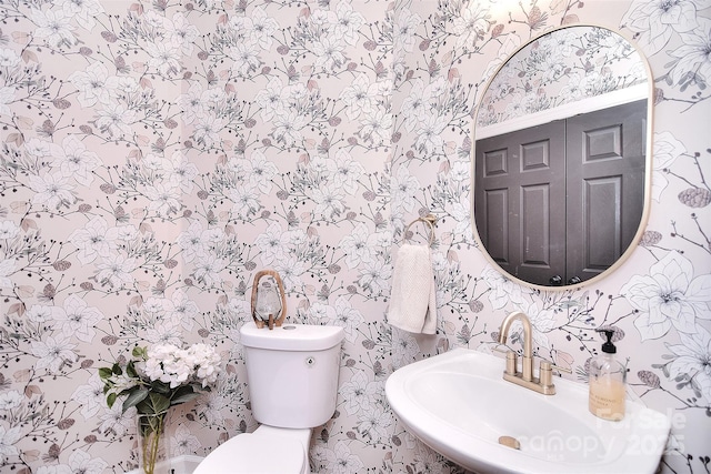 bathroom featuring a sink, toilet, and wallpapered walls