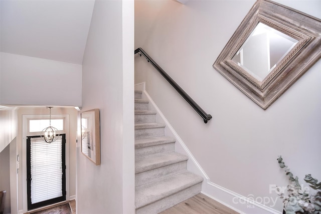 stairway with a chandelier, vaulted ceiling, and wood finished floors