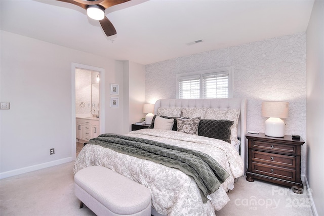 carpeted bedroom with visible vents, a ceiling fan, ensuite bath, baseboards, and wallpapered walls