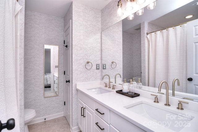 ensuite bathroom with wallpapered walls, a sink, toilet, and tile patterned floors