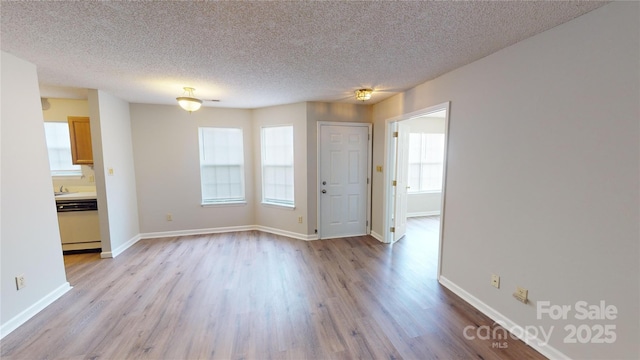 spare room featuring light wood-type flooring, baseboards, and a textured ceiling