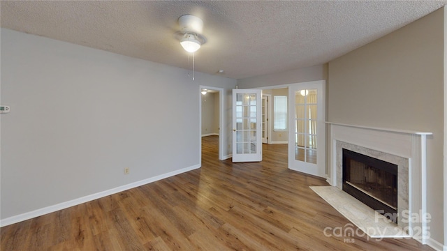 unfurnished living room with a textured ceiling, a premium fireplace, wood finished floors, baseboards, and french doors