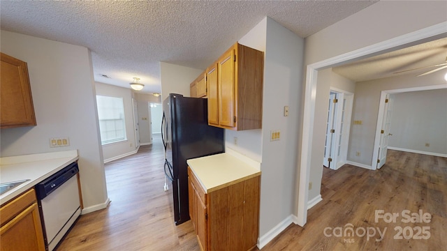 kitchen with freestanding refrigerator, white dishwasher, light countertops, and light wood-style flooring