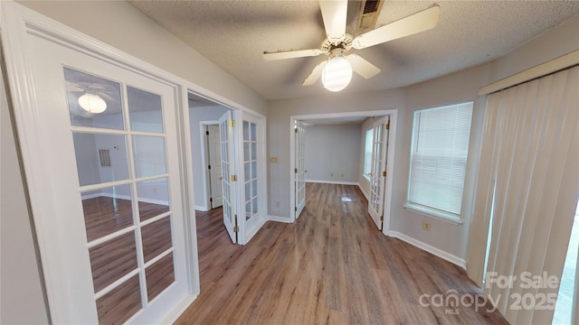 interior space with french doors, a textured ceiling, baseboards, and wood finished floors