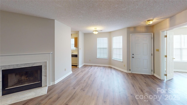 unfurnished living room featuring a textured ceiling, wood finished floors, a high end fireplace, and baseboards