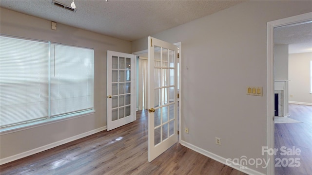 unfurnished room featuring a fireplace with flush hearth, french doors, visible vents, and wood finished floors