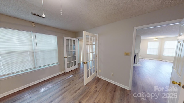 spare room featuring a fireplace with flush hearth, french doors, a textured ceiling, and wood finished floors