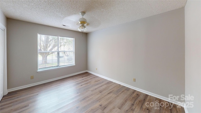 spare room with a textured ceiling, wood finished floors, a ceiling fan, visible vents, and baseboards