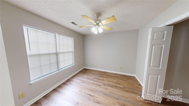 spare room with a textured ceiling, wood finished floors, visible vents, and a ceiling fan