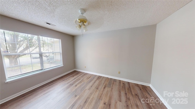 unfurnished room featuring visible vents, a ceiling fan, a textured ceiling, wood finished floors, and baseboards