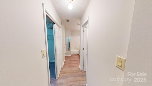 hallway with a textured ceiling and light wood-type flooring