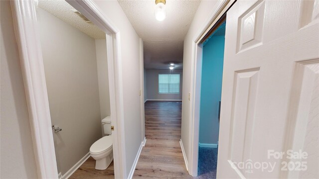 hallway featuring light wood finished floors, visible vents, baseboards, and a textured ceiling