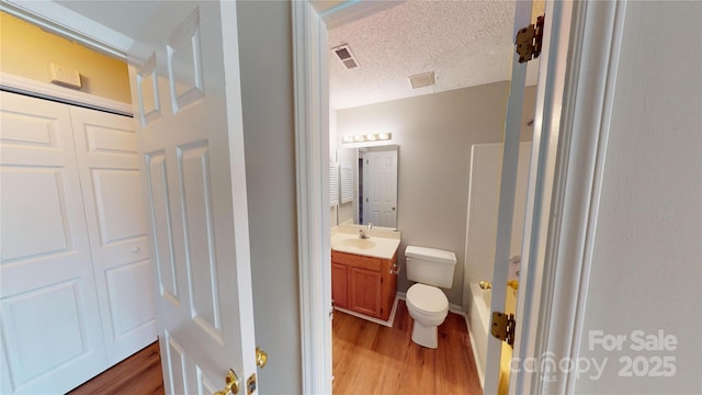 bathroom with toilet, wood finished floors, vanity, and visible vents