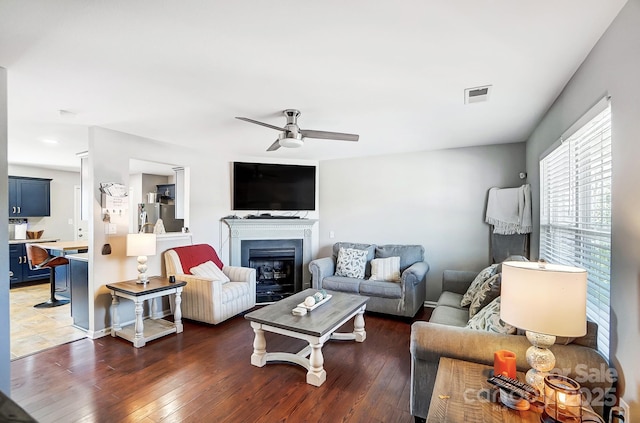 living room featuring a glass covered fireplace, visible vents, ceiling fan, and hardwood / wood-style floors