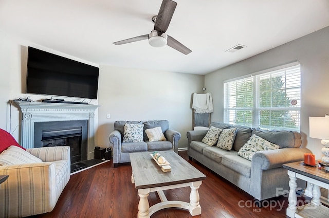 living area with a fireplace with raised hearth, wood finished floors, visible vents, and a ceiling fan