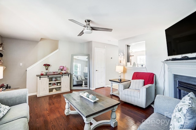 living room featuring a ceiling fan, a fireplace, baseboards, and wood finished floors