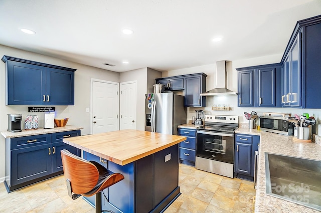 kitchen with blue cabinets, wall chimney range hood, stainless steel appliances, and wooden counters