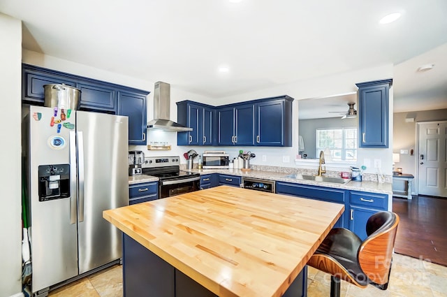 kitchen featuring stainless steel appliances, blue cabinets, a sink, and wall chimney range hood