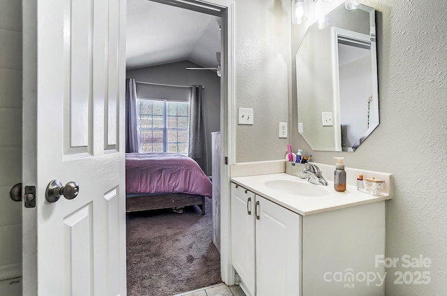 ensuite bathroom with vaulted ceiling, a textured wall, connected bathroom, and vanity