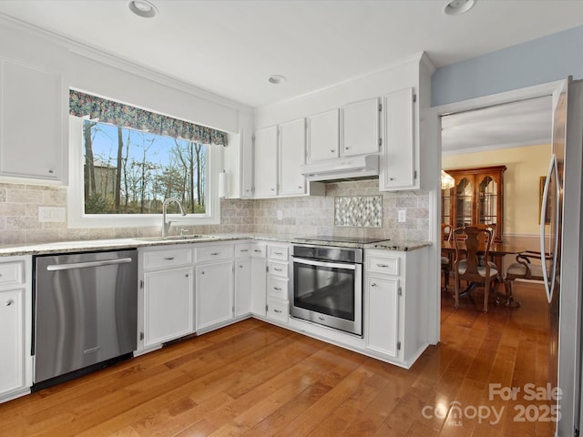 kitchen with a sink, under cabinet range hood, appliances with stainless steel finishes, white cabinetry, and crown molding