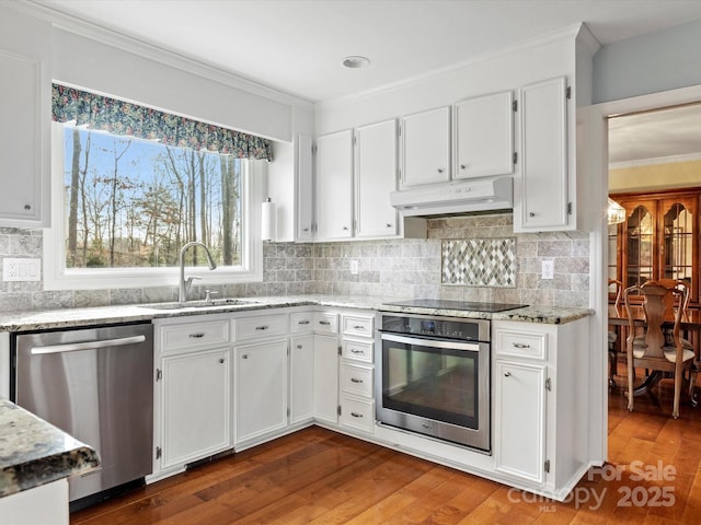 kitchen featuring a sink, ornamental molding, stainless steel appliances, under cabinet range hood, and white cabinetry