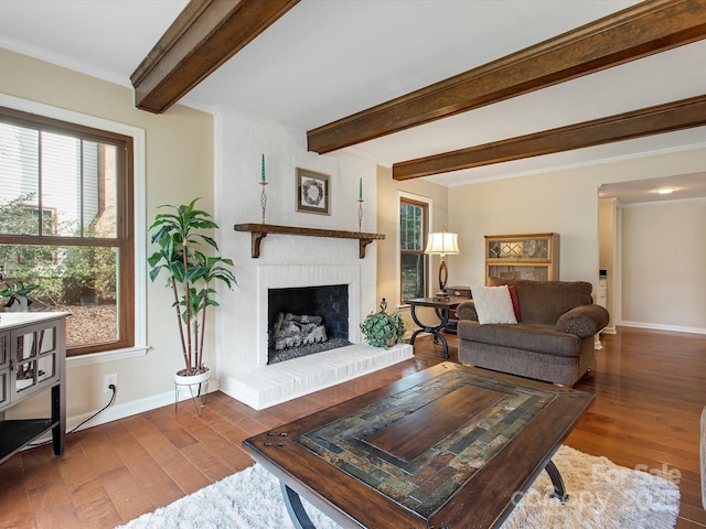 living area with baseboards, beam ceiling, hardwood / wood-style flooring, crown molding, and a brick fireplace