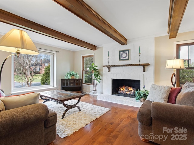 living area with beamed ceiling, a brick fireplace, crown molding, and wood-type flooring