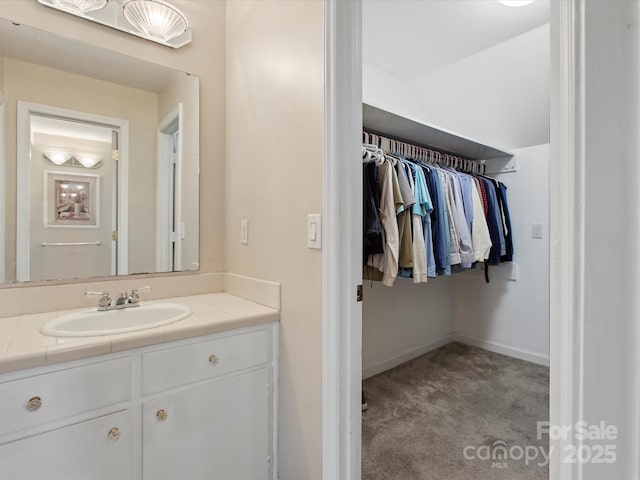 bathroom with a walk in closet, baseboards, and vanity