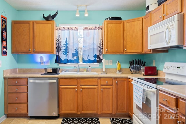 kitchen featuring light tile patterned floors, light countertops, brown cabinetry, a sink, and white appliances