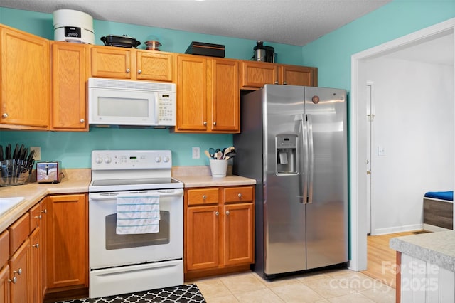 kitchen with white appliances, brown cabinets, light countertops, a textured ceiling, and light tile patterned flooring