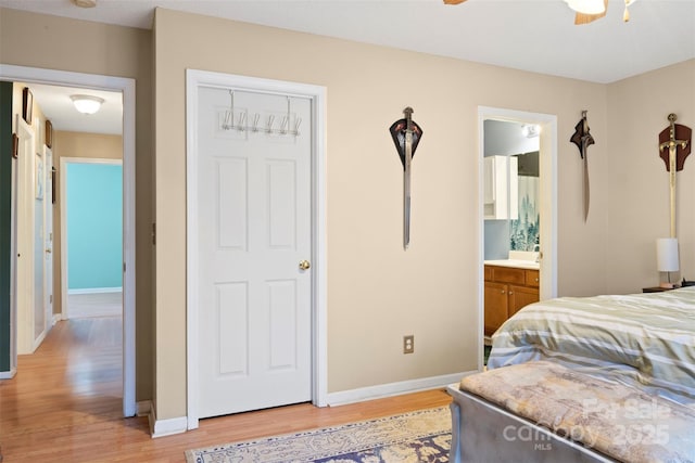 bedroom with light wood-style floors, ensuite bath, and baseboards