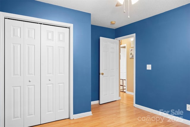 unfurnished bedroom with baseboards, a closet, a ceiling fan, and light wood-style floors