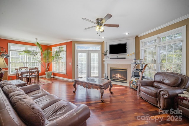 living area featuring ornamental molding, a glass covered fireplace, baseboards, and wood finished floors